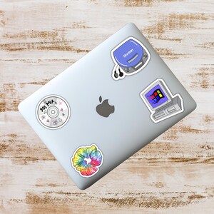 May include: A silver laptop covered in stickers with a 90s theme. Stickers include a blue Discman, a computer with a Windows 95 interface, a tie-dye scrunchie, and a CD with the text "90s Mix".