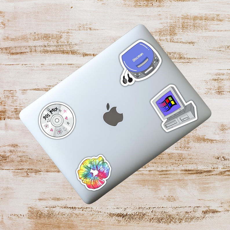 May include: A silver laptop covered in stickers with a 90s theme. Stickers include a blue Discman, a computer with a Windows 95 interface, a tie-dye scrunchie, and a CD with the text "90s Mix".