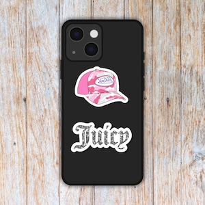 Puede incluir: Una funda de tel&eacute;fono negra con dos pegatinas. La pegatina superior es una gorra de b&eacute;isbol rosa y blanca de camuflaje con el texto "Von Dutch". La pegatina inferior dice "Juicy" en una fuente brillante.