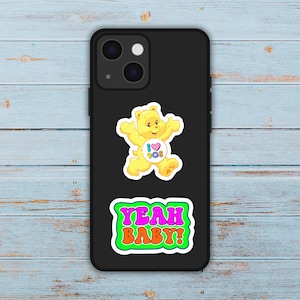 May include: Black phone case with two stickers. The top sticker is a yellow bear with the text "I 90s" in a heart. The bottom sticker says "YEAH BABY!" in pink and orange.