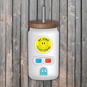 May include: White glass tumbler with a wooden lid and straw. The tumbler is decorated with stickers, including a yellow smiley face with the text "BE KIND PLEASE REWIND", 3D glasses, and a blue ghost.