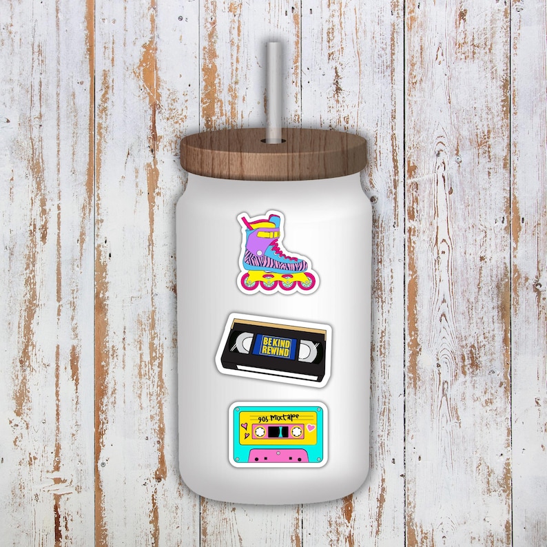 May include: White tumbler with a wooden lid and straw, adorned with stickers. Stickers include a colorful roller skate, a cassette tape labeled "BE KIND REWIND," and a 90s mixtape design.