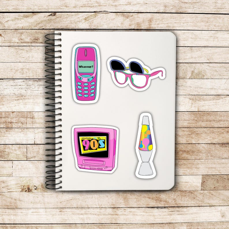 May include: A collection of colorful 90s-themed stickers on a white notebook. Includes a pink flip phone with "Whassup?" text, sunglasses, a pink TV with "90s" text, and a lava lamp.