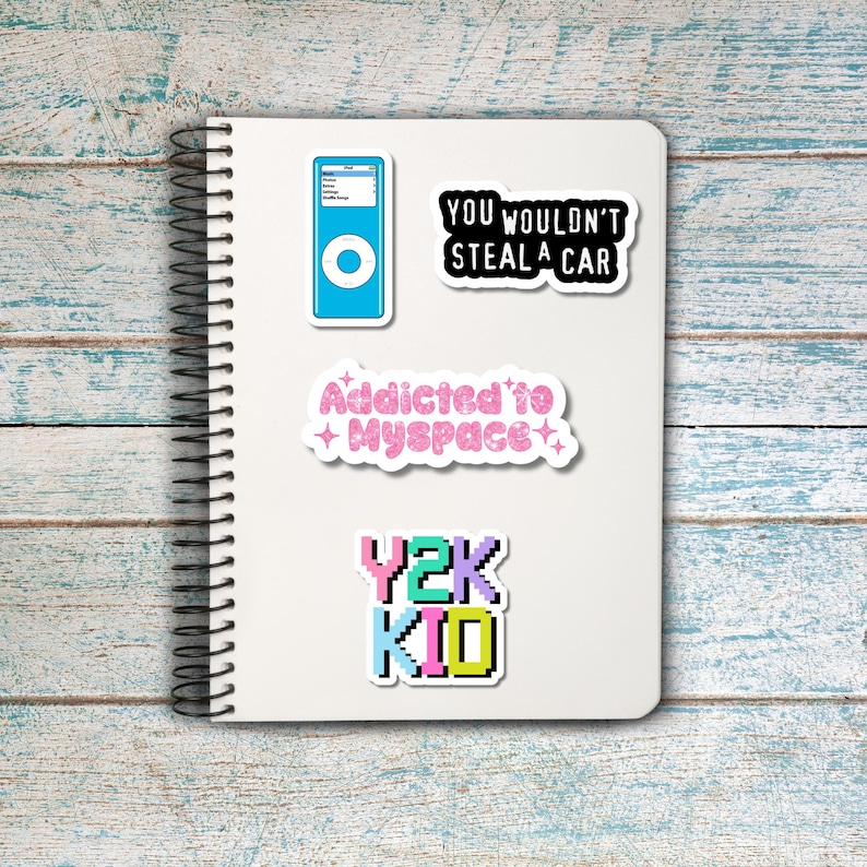 Puede incluir: Un cuaderno blanco con espiral con varias pegatinas. Las pegatinas incluyen un reproductor de MP3 azul, una pegatina negra con el texto "YOU WOULDN'T STEAL A CAR", una pegatina rosa con el texto "Addicted to + Myspace+" y una pegatina colorida que dice "Y2K KID".