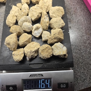 May include: A collection of beige-colored rocks on a black scale, weighing 16.4 oz. The rocks vary in size and shape, with a rough, textured surface. The scale displays the weight in digital numbers.
