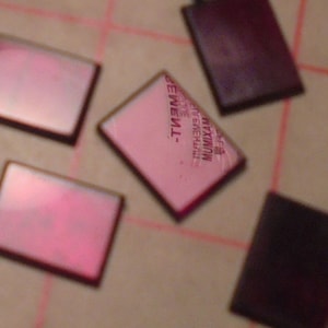 May include: Five small, square, pink and black tiles with a black border. The pink tiles have a white text overlay that reads "MUMIXAM", "EVERGREEN", and "TMT."