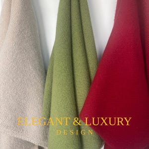 May include: Three draped knitwear items in beige, green, and red. The text "ELEGANT & LUXURY DESIGN" is displayed in gold. The items are hanging against a white background.