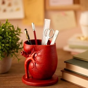 Puede incluir: Una taza de cerámica blanca con un asa negra y el texto "But First, Coffee" en negro, con una fuente de estilo manuscrito. La taza está sobre una superficie blanca.