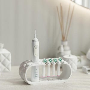 Könnte beinhalten: Eine weiße elektrische Zahnbürste und Ersatzköpfe werden in einem weißen Halter präsentiert. Der Halter hat ein gestepptes Design und hält die Zahnbürste und vier Bürstenköpfe mit grünen Borsten.