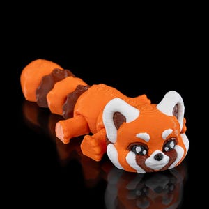 Könnte beinhalten: Eine kleine, orange-braune 3D-gedruckte Rotpanda-Figur mit weißen Gesichtszügen. Die Figur liegt auf dem Bauch und hat den Kopf zur Seite gedreht.