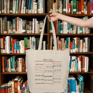 May include: A white canvas tote bag with the text "Date Due" and a grid of dates and years printed on it. The dates are in red.