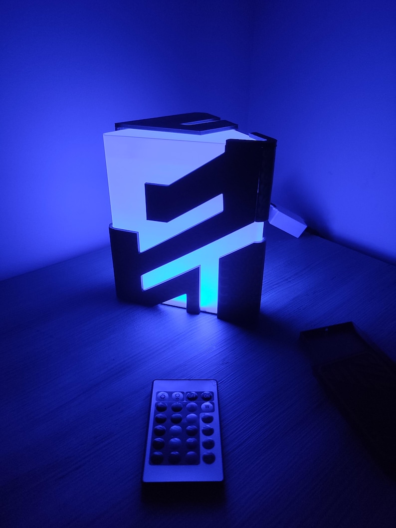 K&ouml;nnte beinhalten: Ein blaues Licht mit einem schwarzen Rahmen und einer Fernbedienung. Das Licht ist in Form eines Buchstabens "F" gestaltet.