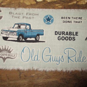 Könnte beinhalten: Ein rechteckiger Aufnäher mit hellblauem Hintergrund und ausgefransten Kanten. Er zeigt eine Illustration eines blau-weißen Pickups, einen Stern und den Text "Old Guys Rule". Zusätzlicher Text enthält "Blast From The Past" und "Durable Goods".