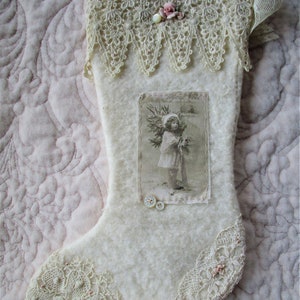 May include: White Christmas stocking with lace trim and a vintage postcard image of a child holding a Christmas tree. The stocking is decorated with small white buttons and pink flowers.