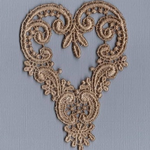 May include: A gold-coloured, heart-shaped lace appliqué featuring detailed floral and scrollwork designs. The lace has a delicate, openwork pattern, suitable for embellishing garments or crafts. The appliqué is set against a light blue background.