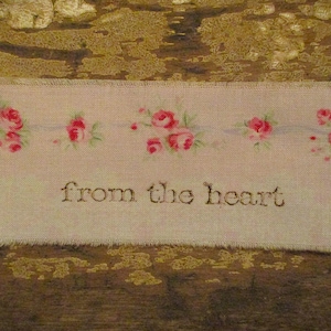 May include: A white fabric with a pink floral pattern and the text "from the heart" embroidered in the centre.