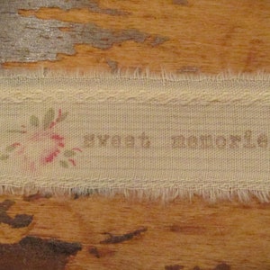 Op de afbeelding: Een wit stoffen label met een roze bloem en groene bladeren die erop geborduurd zijn. Het label heeft de tekst "sweet memories" erop gedrukt.