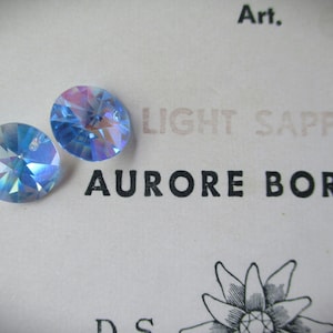 Może przedstawiać: Dwa jasnoniebieskie kryształowe cyrkonie z wykończeniem aurora borealis. Cyrkonie znajdują się na białym tle z nadrukowanym tekstem "LIGHT SAPPHIRE AURORE BOREAL" poniżej.