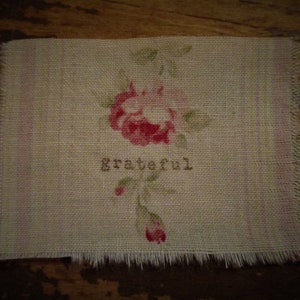 May include: A rectangular burlap patch with a floral design featuring a red rose and green leaves. The word "grateful" is printed in brown letters below the flower. The edges are frayed.