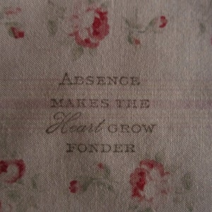 Puede incluir: Una tela beige con un patrón floral y el texto "Absence makes the heart grow fonder" impreso en negro.