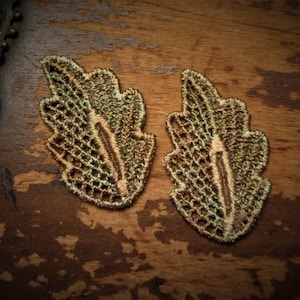 Può includere: Due decorazioni in pizzo a forma di foglia, di colore verde e marrone, su una superficie di legno.