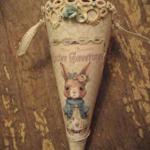 May include: A cone-shaped Easter decoration with a bunny illustration and the text "These Beautiful Easter Greetings". The cone is decorated with lace and a blue flower.