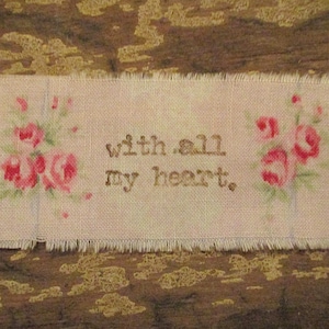 May include: A white fabric tag with pink floral embroidery and the text "with all my heart".