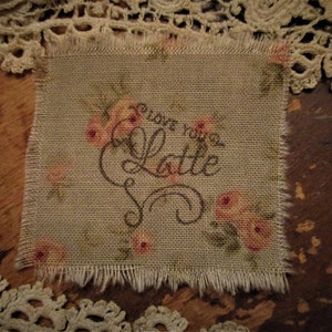 May include: A small, beige fabric square with a frayed edge. It has a floral pattern and the text "love you a latte" embroidered in brown thread.