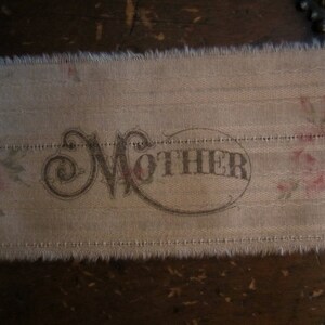 May include: A close-up of a beige fabric with a floral pattern and the word "MOTHER" printed in a cursive font.