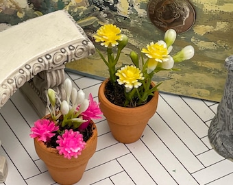 May include: Miniature terracotta pots with colorful artificial flowers. One pot features bright pink blooms, while the other has yellow and white flowers. The pots are set on a white and black herringbone pattern.