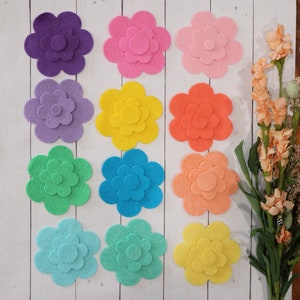 May include: Twelve felt flower shapes in various colors, including purple, pink, yellow, orange, green, blue, and light blue. Each flower has three layers of felt, creating a layered effect.