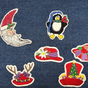 May include: Six embroidered iron-on patches with a Christmas theme. The patches include a crescent moon with a Santa face, a penguin wearing a scarf and hat, a red hat with a white flower, a red hat with a purple bow and antlers, a red hat with a purple bow and a red rose, and a red hat with a green Christmas tree.