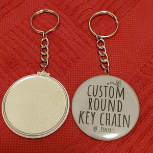 May include: Two silver keychains with round metal tags. One tag is blank and the other has the text "CUSTOM ROUND KEY CHAIN @ _PINPALS" printed on it.