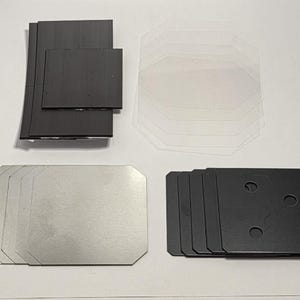 May include: An assortment of various-sized, rectangular and octagonal-shaped components. The components are in shades of black, silver, and clear. Some have rounded corners and some have holes.