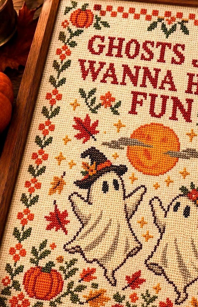 Peut inclure: Une broderie au point de croix dans un cadre en bois repr&eacute;sentant deux fant&ocirc;mes blancs, dont l'un porte un chapeau de sorci&egrave;re, entour&eacute;s de citrouilles orange, de feuilles d'&eacute;rable rouges et d'une pleine lune. Le texte indique GHOSTS WANNA HAVE FUN.