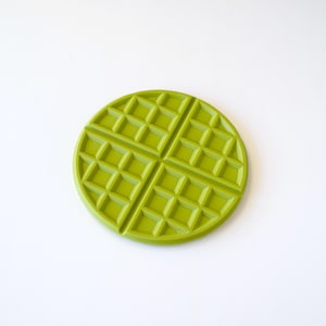 May include: A green waffle-shaped silicone coaster. The coaster is round and has a raised waffle pattern.