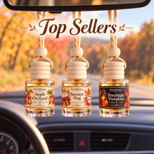 May include: Three glass car diffuser bottles with wooden caps and braided hanging cords. The labels read WaxNWhimsy and feature the scents Apple Orchard, Sweater Hug, and Porchlight Pumpkins. The text Top Sellers is displayed above the bottles.