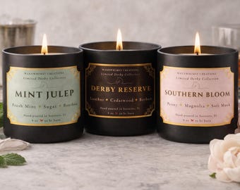 May include: Three black glass candles with lit wicks. Labels read: Mint Julep with notes of Fresh Mint, Sugar, Bourbon; Derby Reserve with Leather, Cedarwood, Bourbon; and Southern Bloom with Peony, Magnolia, Soft Musk. Each is 227g.