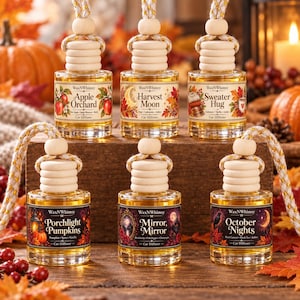 May include: Six glass car diffuser bottles with wooden caps and hanging ropes, each filled with amber liquid. Labels feature the brand WaxNWhimsy and names: Apple Orchard, Harvest Moon, Sweater Hug, Porchlight Pumpkins, Mirror, Mirror, and October Nights.