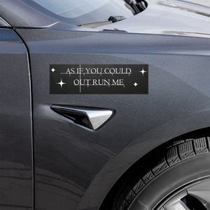 Könnte beinhalten: Schwarzer rechteckiger Autoaufkleber mit dem weißen Text "AS IF YOU COULD OUT RUN ME". Der Aufkleber ist an einem dunkelgrauen Auto angebracht. Der Text wird von Sternenmustern flankiert.