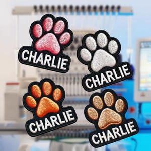 May include: Four embroidered paw print patches with the name "Charlie" written below each paw print. The paw prints are pink, white, orange, and brown.