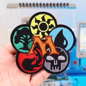 May include: Five embroidered patches featuring the Magic: The Gathering mana symbols. The symbols are yellow, green, blue, red, and black. The patches are arranged in a circle around a large orange letter "M".
