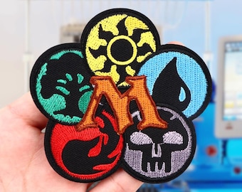 May include: Five embroidered patches featuring the Magic: The Gathering mana symbols. The symbols are yellow, green, blue, red, and black. The patches are arranged in a circle around a large orange letter "M".