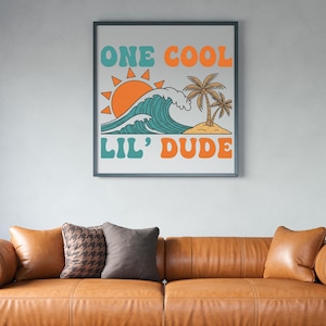 May include: Framed art print featuring a retro design with the text "ONE COOL LIL' DUDE." The artwork depicts a stylized ocean wave, sun, and palm trees in teal, orange, and tan colors. The print is displayed above a brown leather sofa.