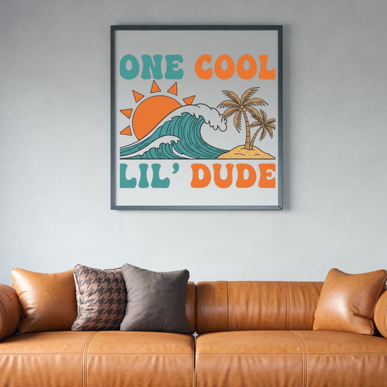 May include: Framed art print featuring a retro design with the text "ONE COOL LIL' DUDE." The artwork depicts a stylized ocean wave, sun, and palm trees in teal, orange, and tan colors. The print is displayed above a brown leather sofa.