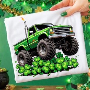 Peut inclure: T-shirt blanc avec un motif de camion monstre vert, de gros pneus et des trèfles. Le camion a un motif de flamme et se détache sur un fond de trèfles verts, parfait pour la Saint-Patrick.