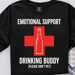 May include: Black sweatshirt with the words "EMOTIONAL SUPPORT" above and "DRINKING BUDDY" below a red cross with a white bottle graphic. The text "[PLEASE DON'T PET]" is below the words "DRINKING BUDDY".