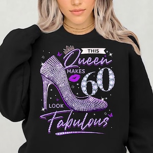 Peut inclure: Sweat-shirt noir avec un motif violet et argenté. Le motif représente une couronne, un escarpin à talon haut et le texte "This Queen Makes 60 Look Fabulous".