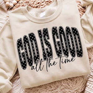 May include: A beige crewneck sweatshirt featuring the black text GOD IS GOOD in a bold, polka-dotted font, with the words all the time written below in a smaller, black cursive script. The garment has long sleeves and a ribbed neckline.