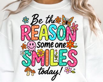 May include: White sweatshirt with a colorful graphic that says "Be the reason someone smiles today!" with flowers, a butterfly, and a smiley face.